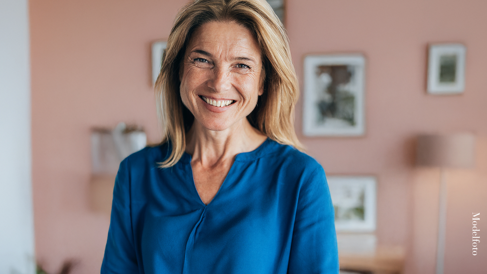 Collagen Shot™ 7 Smilende kvinde ser direkte ind i kameraet i et lyst hjemmemiljø.